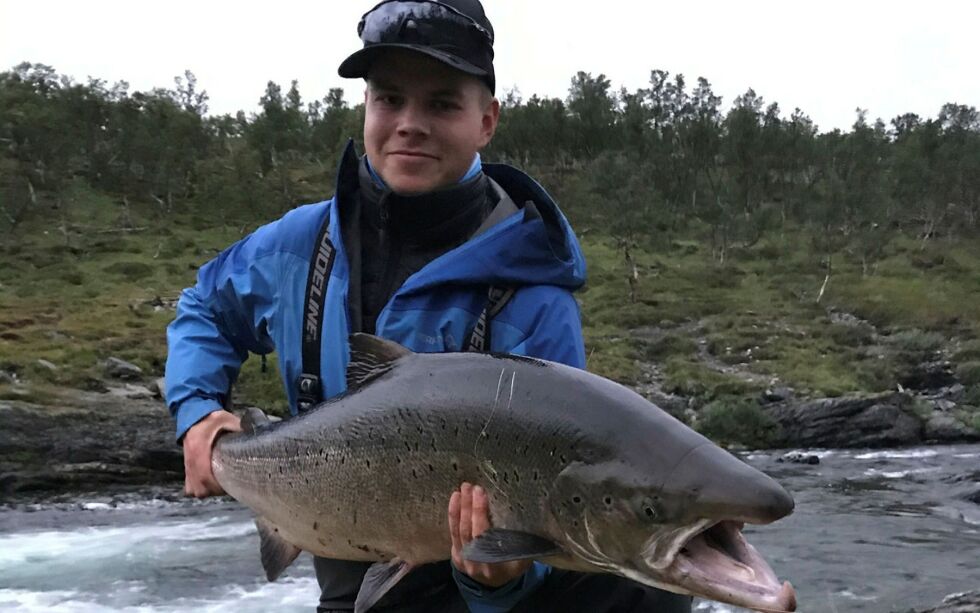 Jovnna Ánde Balto Henriksen fra Tana med storlaksen som ble tatt i Lággojohka/Langfjordelva i helga. Hannlaksen ble veiet til 15 kilo og er sesongens så langt største i den fiskerike elva. FOTO: PRIVAT