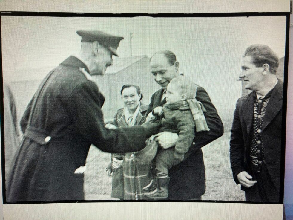 Kong Haakon besøker sørøyværinger i flyktningeleiren Kingston camp i Neilston, nær Glasgow, Skottland. Bildet viser fra venstre kongen som hilser på Berit Mortensen og ektefellen Simon Mortensen med lille Eldor på armen.