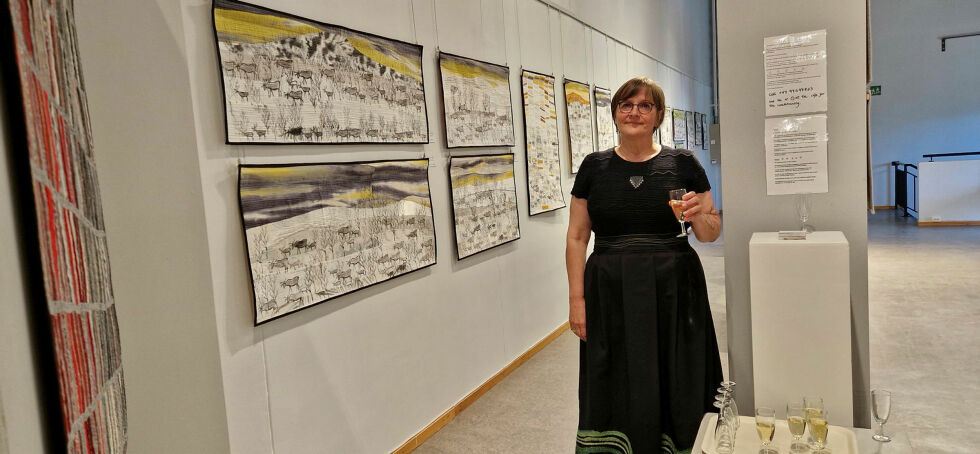 Britt Inger Berntsen foran en lang vegg av tepper med reintema.
 Foto: Hill Haga