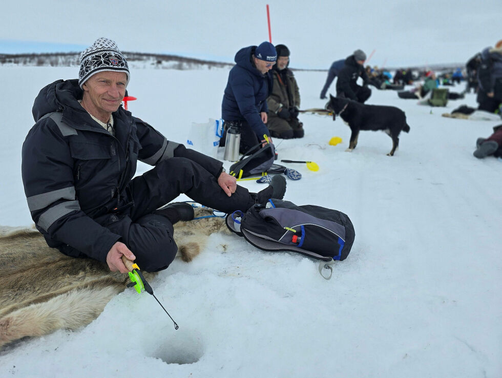 Bjørn Frode Fagerhaug fra Måsøya trives med pilkestikka og en god kopp kaffe ute på isen. Han ser ikke mørkt på tilværelsen, selv om det blåser litt sur nordavind og fisken glimrer med sitt fravær på Láhpojávri.
 Foto: Yngve Beddari
