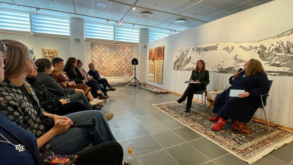 Hilde Skancke Pedersen i samtale med førstekonservator Maria Øien ved Alta museum. Pedersen er fylt 72 år, men er i full aktivitet. Til høsten skal hun levere et seks meter langt teppe til det nye regjeringskvartalet, med motiv av hellig fjell. Ganske likt teppet bak de to.
 Foto: Rita Heitmann