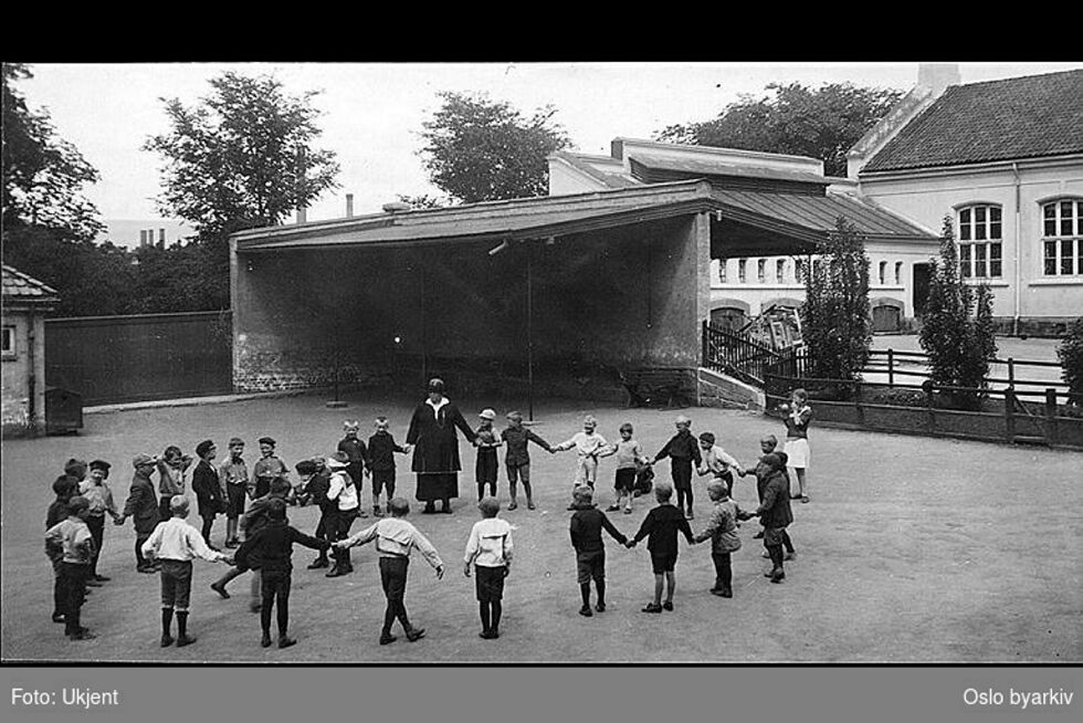 Lærer og forfatter Regine Normann i lek med klassen i skolegården.  Fra albumet «Sofienberg skole femti år - 1. september 1933.»
 Foto: Ukjent fotograf, Oslo byarkiv