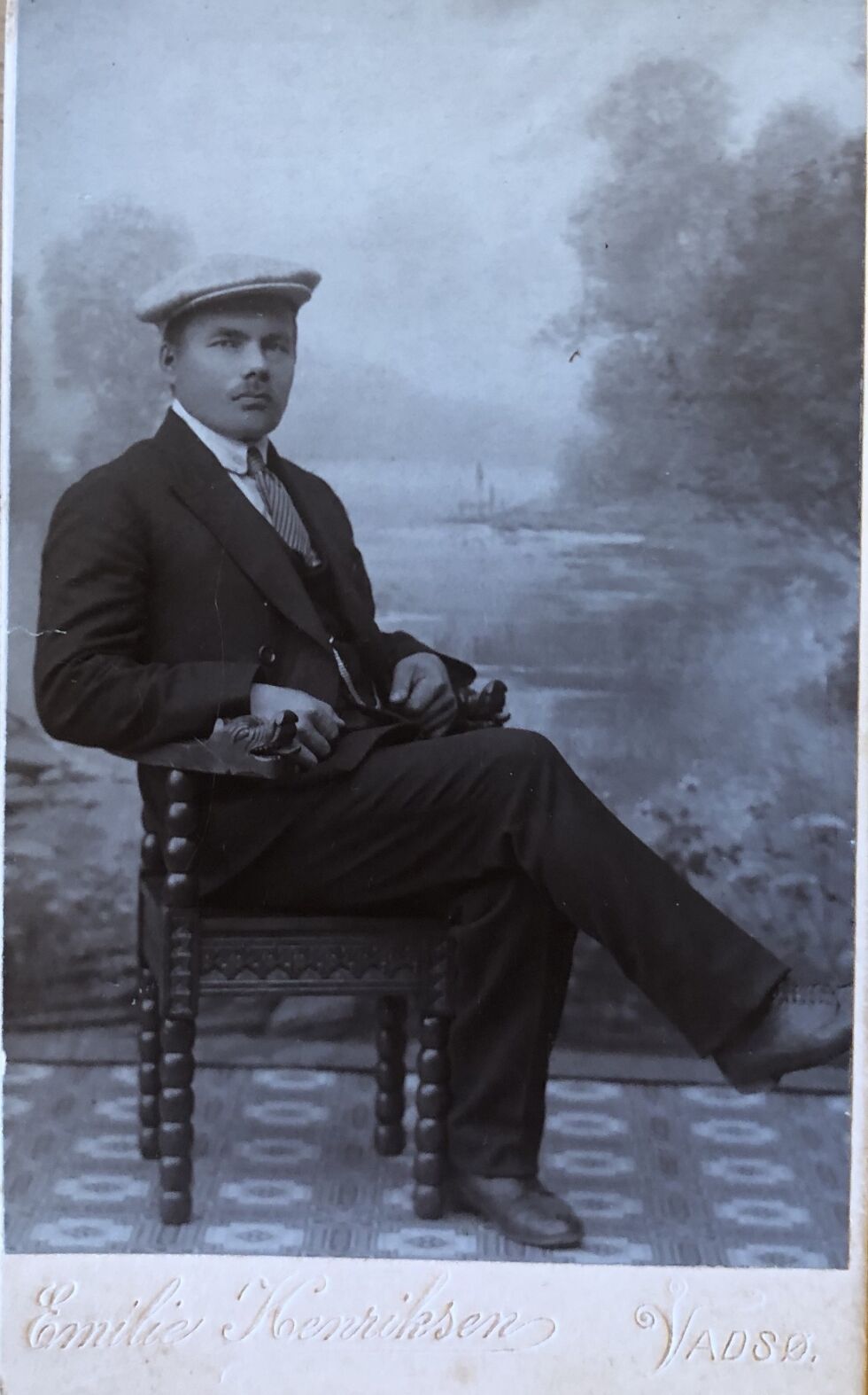 Et idyllisk landskap i bakgrunnen i fotografens studio, og en pent kledd mann poserer.
 Foto: Emilie Henriksen