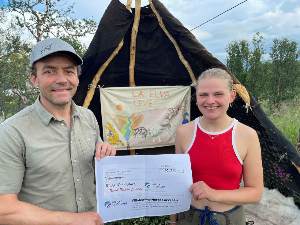 Vegard Heggem fra Norske Lakseelver overrekker gavesjekk på 10.000 kr til aktivist Åsa Braut Backe. I bakgrunnen lavvoen med banneret fra Alta-kampen.
 Foto: Norske Lakseelver