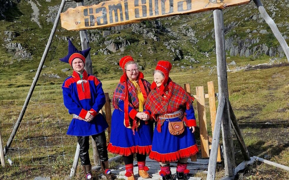 Tre generasjoner poserer så fint foran skiltet til leiren, «Sámi Siida». Fra venstre Nils Mathis Sara, Marit Gunhild Sara og Marit Anne Eira Sara.
 Foto: Charlotte Iselin Mathisen