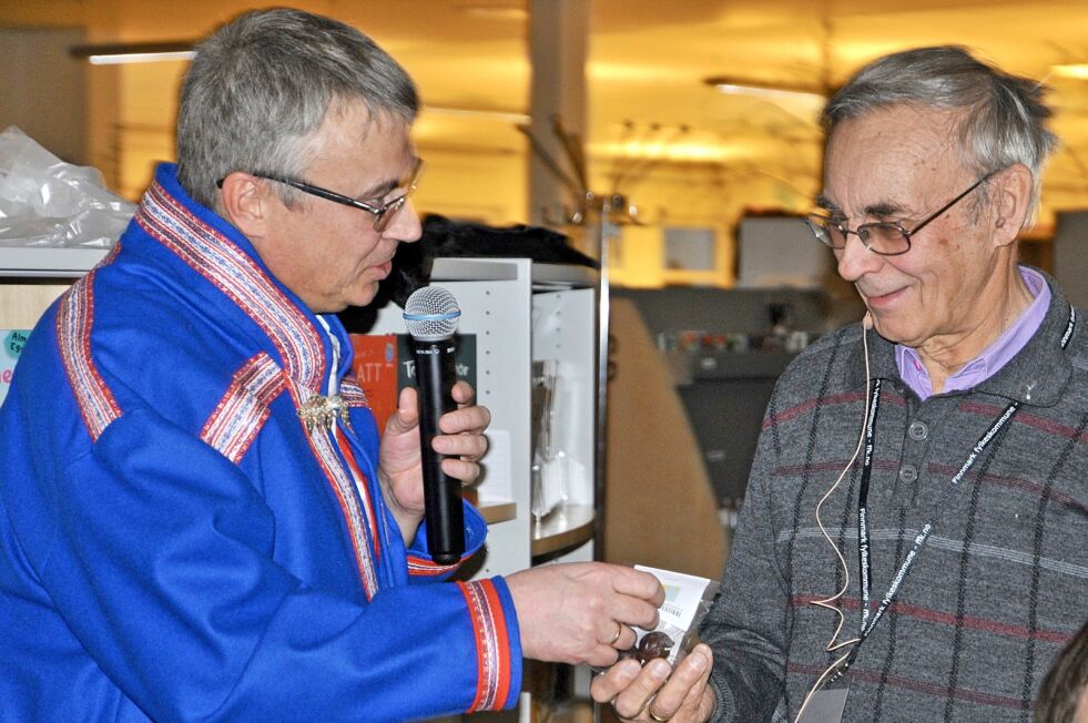 Odd Mathis Hætta får en gave fra John Harald Skum ved Alta bibliotek under Finnmark internasjonale litteraturfestival, som takk for foredrag om samiske offerplasser i Alta.
 Foto: Rita Heitmann