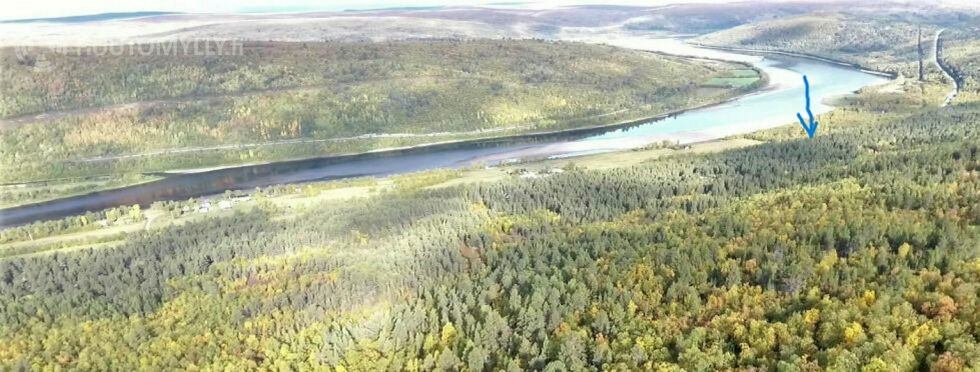 Tanaelva med Norge og E6 til venstre og Finland og RV 970 til høyre. Stedet hvor hytta i Biesjohka ligger er markert med blå pil.
 Foto: Skjermdump