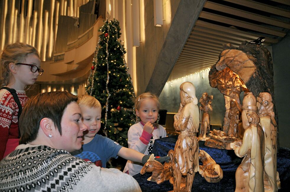 Marie Louise Hætta Lantto har med seg sinn sønn Lemet Áilu på fire år, og niese Marit Anne på fem, til den samiske gudstjenesten i nordlyskatedralen. Her studerer de julekrybben, sammen med Anastasia.
 Foto: Rita Heitmann