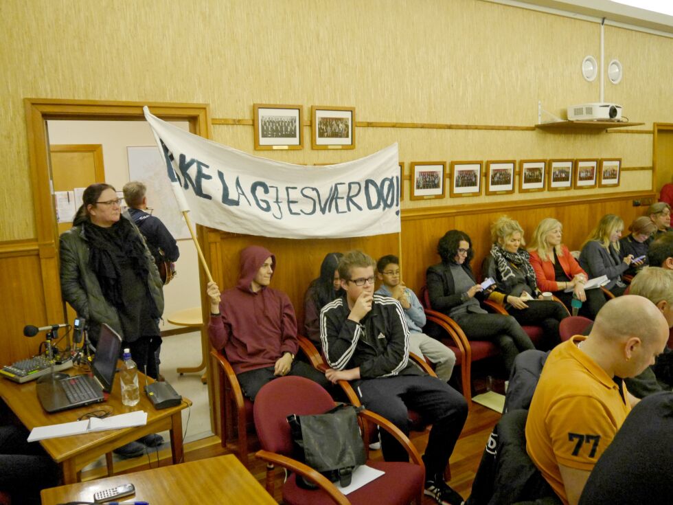 Fra Gjesvær skole møtte man opp med protestfane, da kommunestyret i Nordkapp tirsdag enstemmig gikk imot rådmannens forslag om å overføre ungdomstrinnet ved skolen til Honningsvåg. Elevene David Vian og Nathawat Sonhom holder fanen, Pimtawan Sonhom sitter mellom dem, mens Marcus Walsøe sitter foran. Til venstre står rektor/lærer Helene Walsø Kanstad. Flere tilhørere hadde også møtt opp i rådhussalen i Honningsvåg tirsdag.
 Foto: Geir Johansen