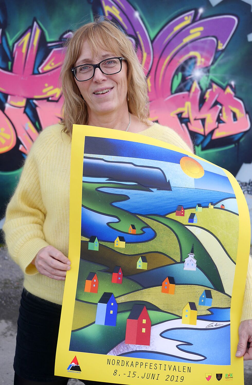 Festivalsjef Edelh Ingebrigtsen med årets fargesterke plakat for Nordkappfestivalen, som er laget av EvArt, som Eva Schmutterer driver i Kamøyvær og i Honningsvåg. – Vi satser på en glad festival med god feststemning i juni, sier Edelh.
 Foto: Geir Johansen